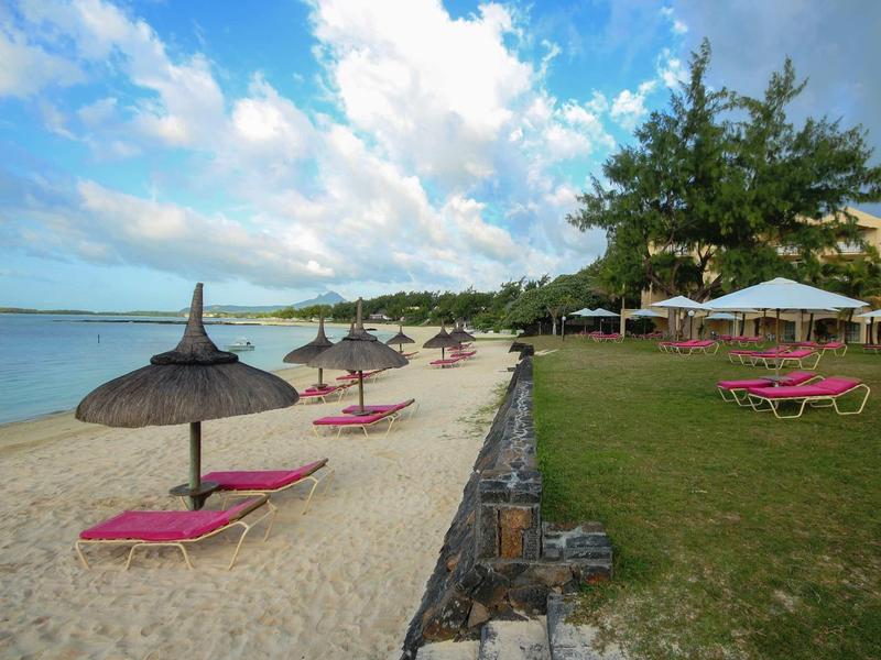 Spiaggia con ombrelloni di paglia, lettini rossi e prato verde accanto alla sabbia