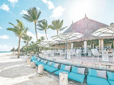 Strandrestaurant mit Palmen, weißen Sonnenschirmen und blauen Sitzkissen am Sandstrand.