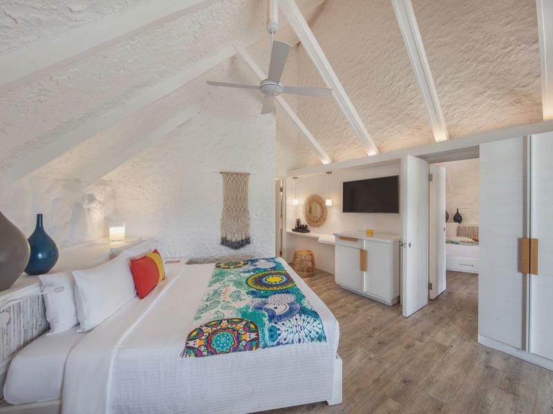 Gezellige hotelkamer met witte muren, houten vloer, tweepersoonsbed, plafondventilator en tv.