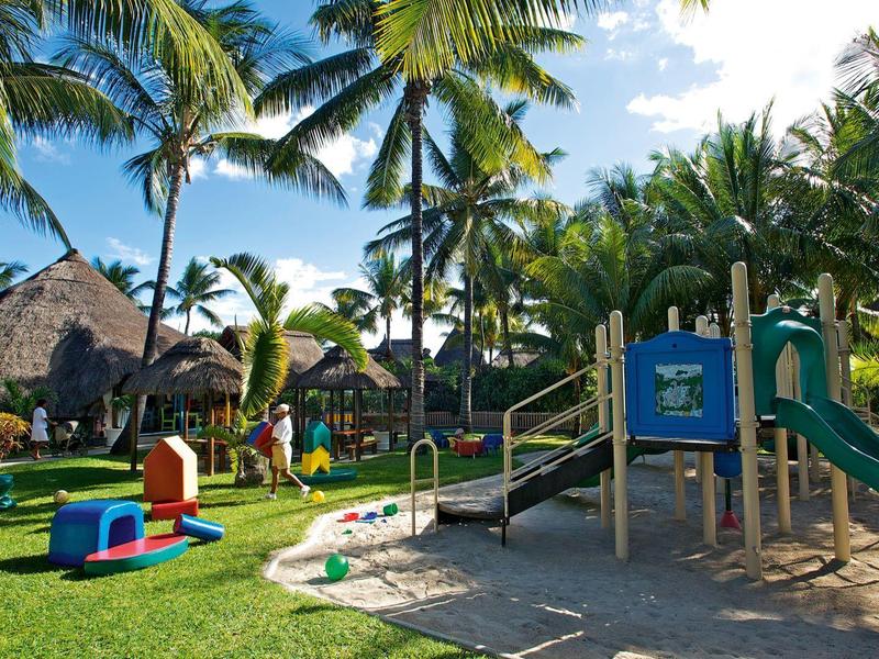 Zonnige tropische speeltuin met glijbanen en palmbomen bij een vakantieoord.