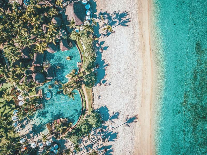Luchtfoto van een tropisch strandresort met palmbomen, zwembaden, zandstrand en turquoise zee.