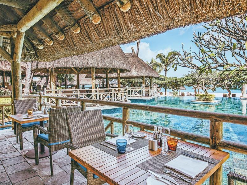 Buitenterras met rieten dak bij een zwembad, omgeven door tropische planten.