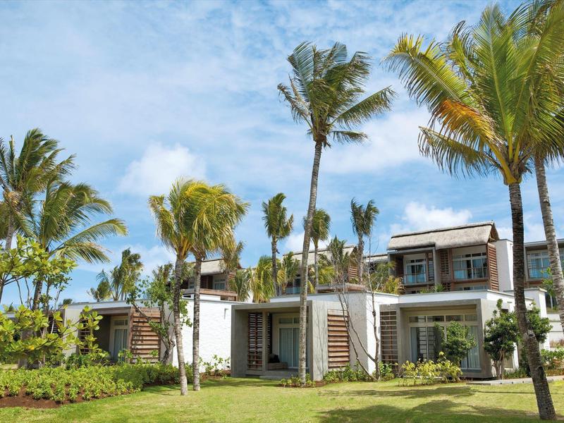 Modern resortgebouw omgeven door palmbomen onder een gedeeltelijk bewolkte hemel.