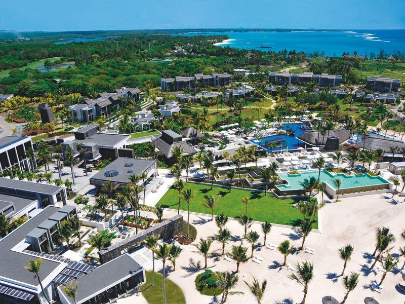 Luchtfoto van een tropisch strandresort met zwembaden, palmbomen en wit zandstrand.