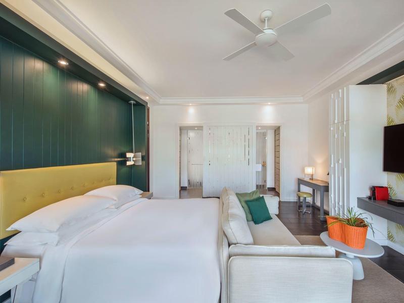 Hotelkamer met twee eenpersoonsbedden, groene accentmuur, wit plafondventilator en een gezellige fauteuil.