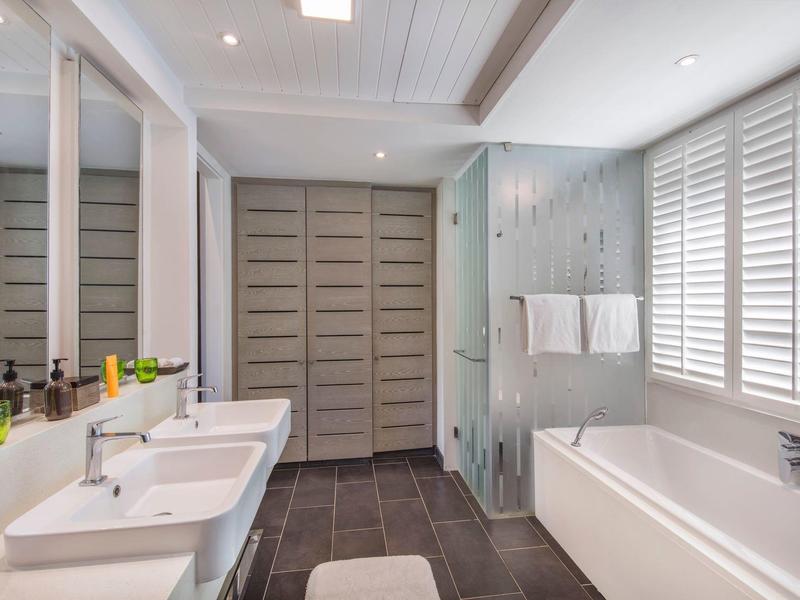 Moderne badkamer met dubbele wastafels, badkuip en grote kasten achter schuifdeuren.