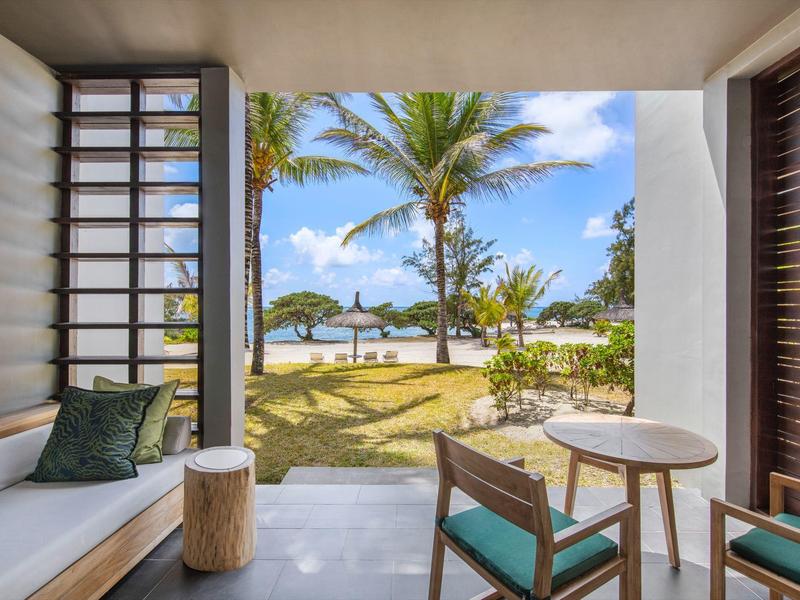 Gezellig terras met stoelen en bank met uitzicht op palmbomen en zonnig strand.