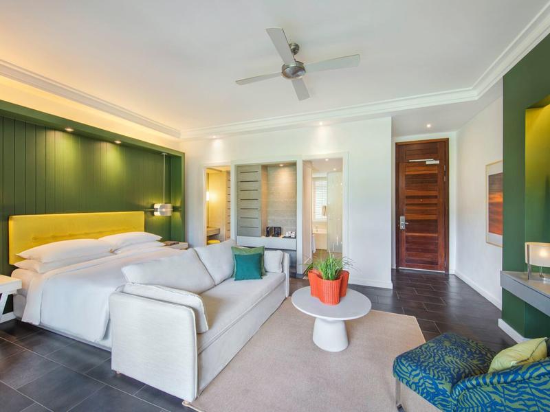 Lichte hotelkamer met bed, zithoek, groene accentmuur en moderne inrichting.