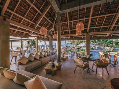Área de salón abierta con muebles de madera y vistas a una piscina en entorno tropical.