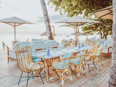 Venkovní restaurace s dřevěnými stoly, židlemi a slunečníky s výhledem na moře.