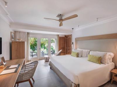 Habitación de hotel luminosa con cama grande, escritorio, silla y vista a una terraza con verde.