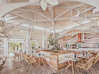 Área de restaurante de hotel luminosa y abierta con muebles de madera y mimbre y grandes ventanas.