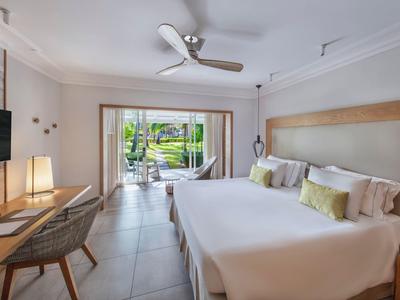 Habitación de hotel moderna con cama doble, ventilador de techo y vista a una terraza con jardín.