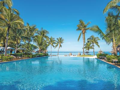 Velký bazén s palmami u moře pod jasně modrou oblohou.