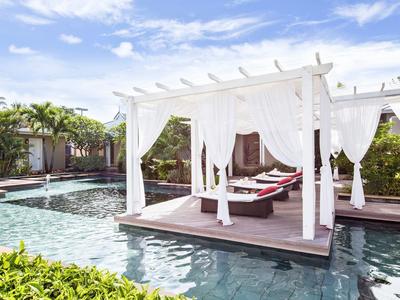 Área de piscina con camas dosel blancas y cojines rojos en un hotel tropical.