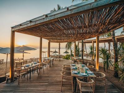 Otevřená restaurace s dřevěnou podlahou s výhledem na pláž a moře při západu slunce.