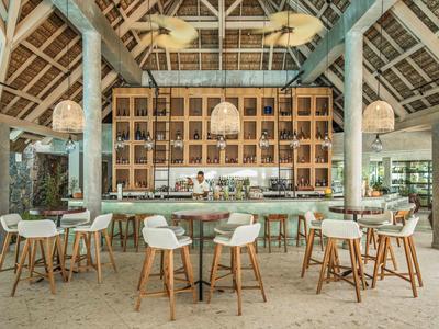 Área de bar moderna en hotel con taburetes de madera y techo abierto de madera y hojas de palma.