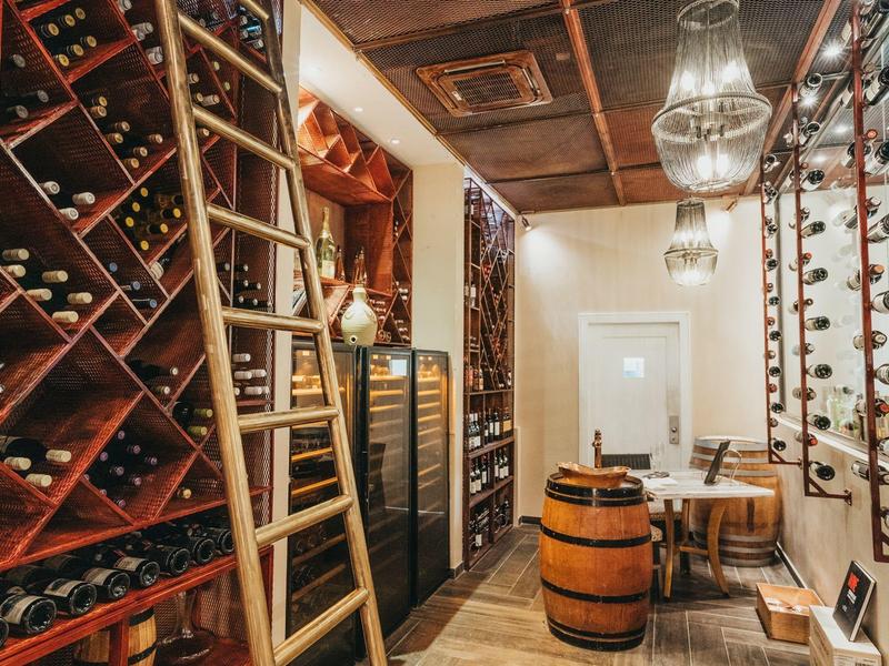 Bodega con estanterías de madera, botellas, escalera y barril rústico como mesa en hotel.