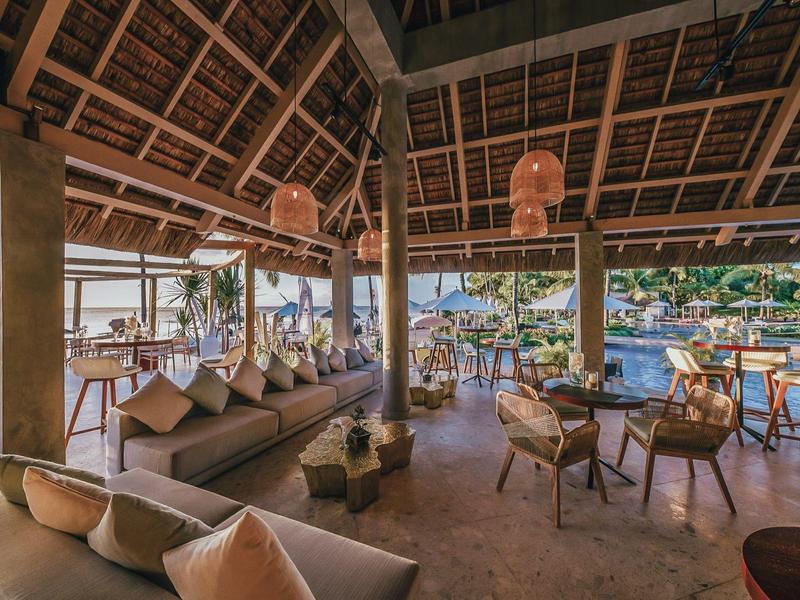 Área de salón abierta con muebles de madera y vistas a una piscina en entorno tropical.