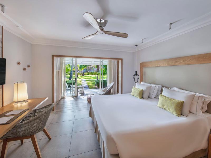 Habitación de hotel moderna con cama doble, ventilador de techo y vista a una terraza con jardín.