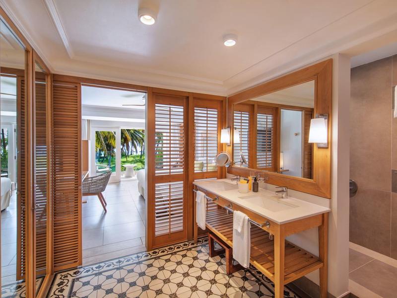 Baño moderno con detalles de madera, lavabo doble y acceso a una sala de estar luminosa.