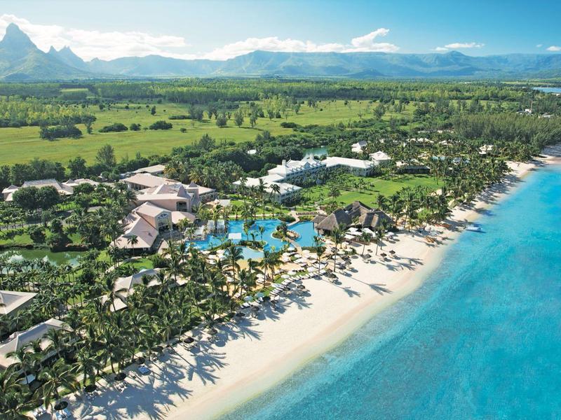 Vista aérea de un resort tropical en la playa con mar azul, arena y palmeras.