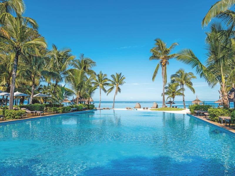 Gran piscina del hotel con palmeras y vista al mar bajo un cielo azul despejado.