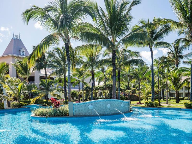 Gran piscina del hotel con palmeras y terraza soleada bajo cielo despejado.