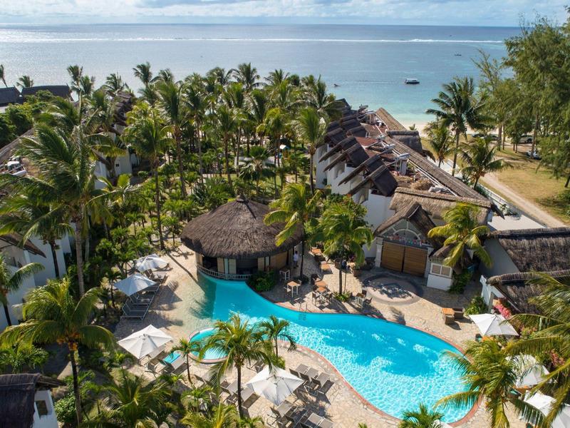 Resort con piscina blu, circondato da palme e ville tropicali vicino alla spiaggia.