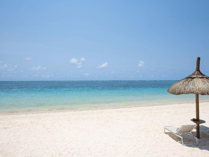 Spiaggia soleggiata con cielo azzurro limpido, mare calmo e ombrellone di paglia con lettini.