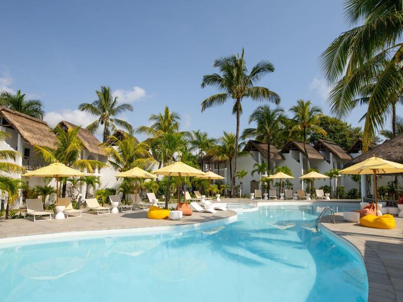 Area piscina del resort con palme, ombrelloni gialli e lettini sotto cielo sereno.