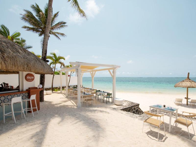 Bar sulla spiaggia con palme, ombrelloni di paglia e tavoli su sabbia bianca vicino al mare turchese.