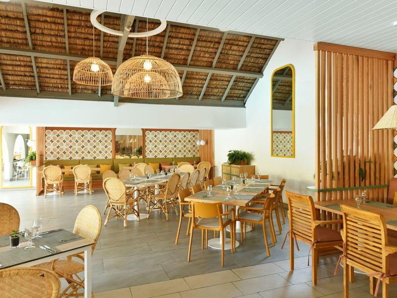 Area pranzo con sedie in legno, tavoli e lampade rattan sotto un soffitto alto in legno.