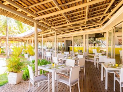 Überdachte Terrasse mit weißen Stühlen und Tischen, umgeben von Pflanzen und Holzboden.