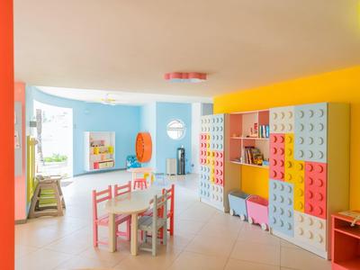 Buntes Kinderspielzimmer mit Lego-Wand, bunten Möbeln, Tischen und Stühlen in hellem Raum.