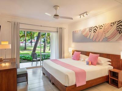 Modernes Hotelzimmer mit großem Bett, rosa Akzenten und Blick auf tropischen Garten.