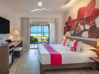 Modernes Hotelzimmer mit großem Bett, roter Dekoration und Blick auf den Strand durch Fenster.