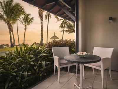 Balkon mit Tisch und zwei Stühlen, Palmen und Meer im Hintergrund bei Sonnenuntergang.