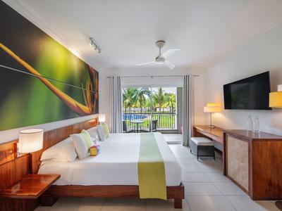 Modernes Hotelzimmer mit Doppelbett, Holzmöbeln, großem Fenster und Blick auf Palmen.