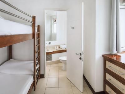 Kleines Hotelzimmer mit Etagenbett, offenen Tür zum Badezimmer und Kommode neben Fenster.