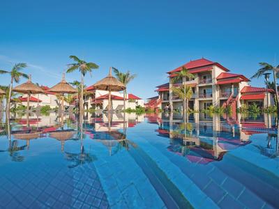 Großer Hotelpool mit Palmen und roten Dächern unter klarem blauem Himmel.