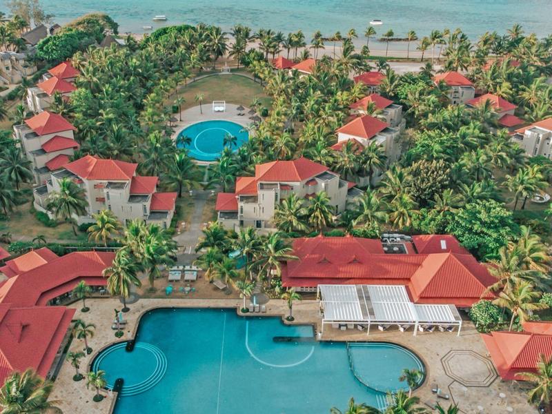 Luxuriöse Resortanlage mit großen Pools, roten Dächern, vielen Palmen und Meer im Hintergrund.