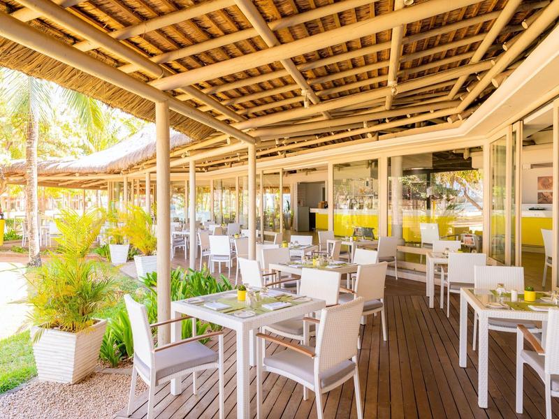 Überdachte Terrasse mit weißen Stühlen und Tischen, umgeben von Pflanzen und Holzboden.