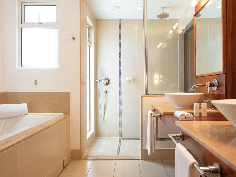 Modernes Badezimmer mit weißer Badewanne, Glastür zur Dusche, Holzregal und Waschbecken.