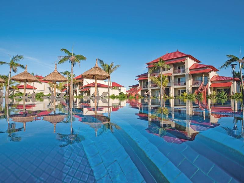 Resort mit roten Dächern, Palmen und großem blauem Pool unter klarem Himmel.