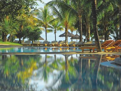 A calm pool area with palm trees, sun loungers, and umbrellas by the beach.