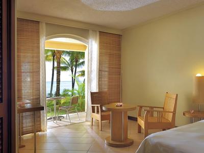 Helles Hotelzimmer mit Holzmöbeln und Blick auf tropischen Garten und Meer.