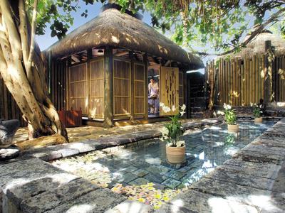 Traditional thatched huts with a small pond and trees in a peaceful garden.