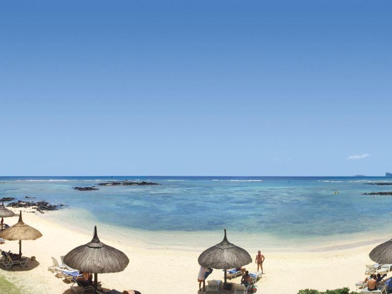 White sandy beach with palm trees, thatched umbrellas, and clear blue sea under a clear sky.