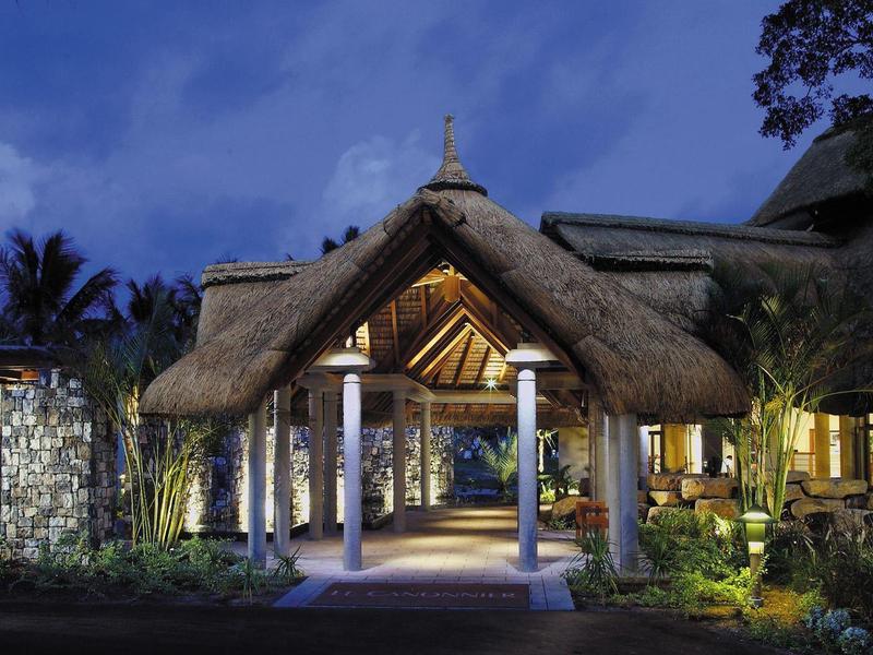 Entrance of a tropical resort with thatched roof and illuminated paths at night.